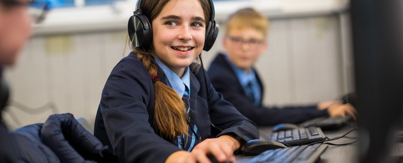 Student with headphones on working at a PC desk, with a mouse in her hand