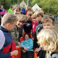 students crowded around a girl in an orange bag being carried